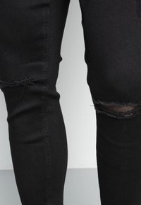 Svarta tajta jeans med en sliten design och revor vid knäna, gjorda av denimtyg med en mjuk textur och fin sömnad.