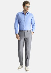 Camisa de botones azul claro, pantalones gris ajustados con un patrón sutil y zapatillas beige. El conjunto presenta un diseño moderno y entallado.