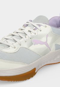 Λευκό και ανοιχτό μωβ αθλητικό παπούτσι Puma με δίχτυ, λευκά κορδόνια και σόλα χρώματος καουτσούκ σε απλό φόντο.