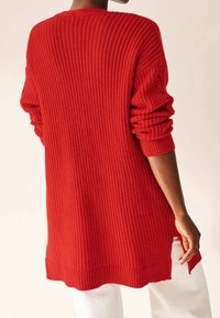 Maglione rosso lavorato a maglia con texture a costine, maniche lunghe e spacchi laterali. Lunghezza media, vestibilità rilassata e colore uniforme senza ulteriori motivi.