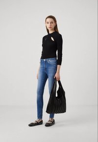 Top negro de manga larga acanalado con cortes, jeans ajustados azules, bolso bandolera negro con pliegues y zapatos planos negros con lunares blancos y tachuelas.