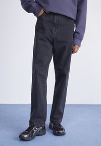 Svarta denimjeans med rak bendesign, med sidofickor och en diskret textur. Matchat med svarta sportskor.
