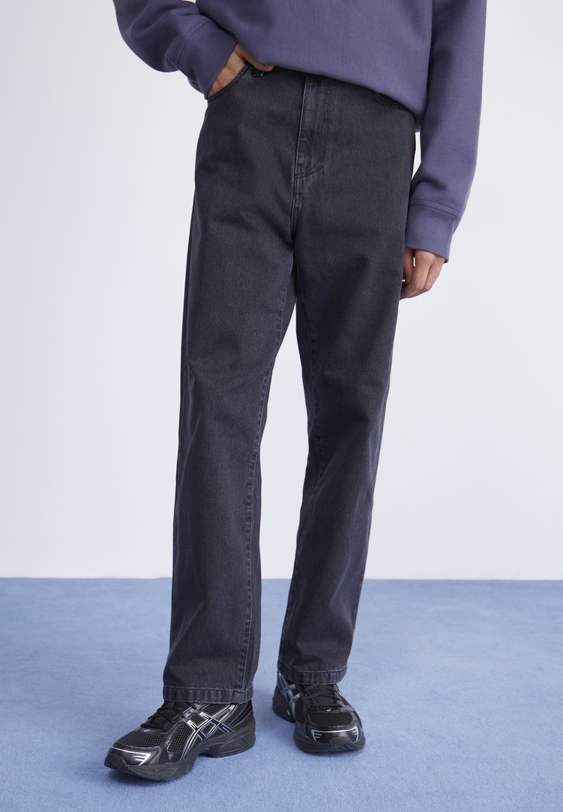 Sorte denimbukser med rett ben-design, med sidelommer og en subtil tekstur. Kombinert med sorte joggesko.