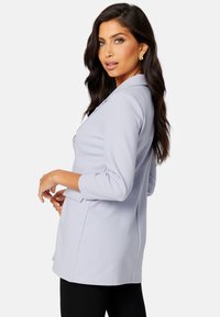 Blazer azzurro chiaro con design classico, vestibilità su misura e maniche a tre quarti, caratterizzato da tasche a patta e una texture liscia.