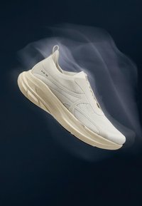 Baskets de sport blanches légères avec une semelle épaisse et rembourrée, suspendues sur un fond sombre avec un effet de mouvement translucide.