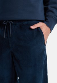 Marine corduroy joggings met een gestructureerd oppervlak, elastische tailleband en zijzakken. Koordaccenten bij de taille.