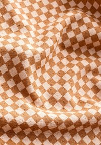 Tissu à carreaux brun et crème avec une texture douce. Le motif consiste en des carrés alternés, créant une apparence tissée et chaleureuse.