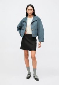 Niebieska krótka kurtka z kołnierzem i dwoma przednimi kieszeniami, na beżowym swetrze, w połączeniu z czarną spódnicą i szarymi, sięgającymi kolan skarpetami.