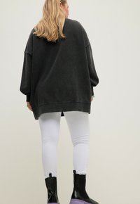 Överdimensionerad mörkgrå sweatshirt med sänkta axlar, kombinerad med vita åtsittande leggings och svarta ankelstövlar med lila sulor.