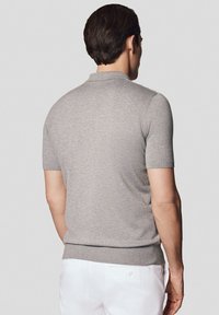 Szary polo sweter z krótkim rękawem, z prążkowanym kołnierzykiem i dołem, o gładkiej fakturze i dopasowanym kroju, połączony z białymi spodniami.