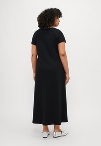 Czarna, krótko rękawowa sukienka maxi o luźnym kroju. Materiał jest gładki, a design charakteryzuje się prostą, czystą sylwetką. Do sukienki pasują srebrne buty.