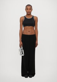 Black sports bra with silver detailing, high-waisted black trousers, and a small silver handbag. Smooth texture and tailored fit.