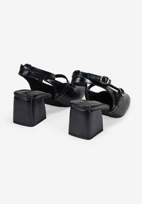 Escarpins noirs en cuir avec un talon carré, une sangle ajustable à la cheville et une texture lisse, présentant un design minimaliste.