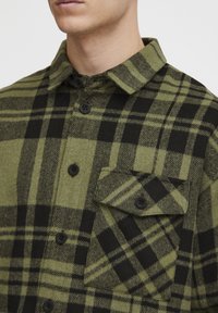 Groene en zwarte geruite flanellen overhemd met een knoop-kraag, een borstzak en zwarte knopen. Zachte textuur en geruit patroon.