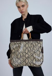 Grote boodschappentas met een nepslangenhuidpatroon, beige en bruine tinten, leren afwerking en handvatten van bamboe. Ruimtelijk en gestructureerd ontwerp.
