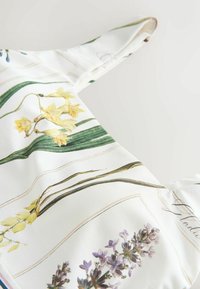 Tissu blanc avec des illustrations botaniques imprimées de fleurs jaunes et violettes et de feuilles vertes, avec un détail de bretelle.