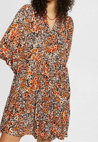 Blumenkleid mit schwarzem Hintergrund, ausgestattet mit orangefarbenen und weißen Blumen, einem V-Ausschnitt und Dreiviertelärmeln. Aus Baumwollstoff, locker geschnitten.