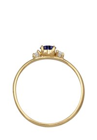 Bague en or avec une pierre précieuse bleue centrale, accentuée par deux petites pierres claires de chaque côté, dotée d'un bandeau lisse et poli.