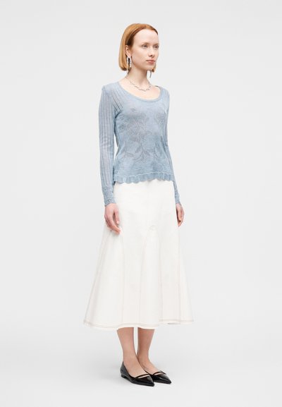 Pull en tricot bleu clair avec motif floral, manches longues et ourlet festonné, associé à une jupe blanche trapèze et des chaussures plates noires.