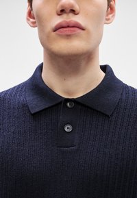 Pólo azul marinho com um design texturizado em canelado, apresentando um colarinho clássico e uma tapeta de três botões, feito de um tecido de malha suave.