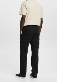 Svarta cargobyxor med flera sidofickor, tillverkade av slitstark tyg. Bärs med en beige t-shirt, som har en avslappnad passform och rak bendesign.