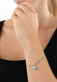 Bracciale in argento con un ciondolo tondo in turchese. Il ciondolo ha una texture liscia e un accento metallico, caratterizzato da un design minimalista.