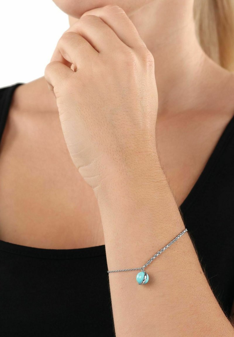 Bracciale in argento con un ciondolo tondo in turchese. Il ciondolo ha una texture liscia e un accento metallico, caratterizzato da un design minimalista.
