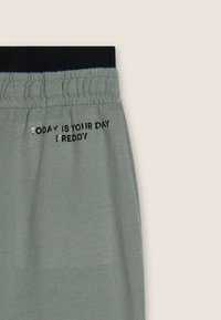 Joggers gris claro con una cintura elástica negra. Presentan el texto plateado "HOY ES TU DÍA FREDDY" a lo largo del costado. Textura suave y lisa.