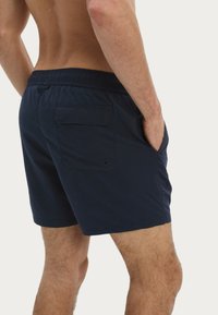 Bañador azul marino hecho de tejido ligero, con un cinturón elástico, bolsillos laterales y un bolsillo trasero con botón.