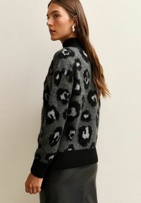 Suéter de estampado de leopardo en negro y gris, hecho de un material de punto suave; cuenta con un cuello y puños acanalados en negro, con un corte holgado.