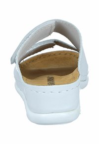 White slip-on shoe with a textured leather upper, a cushioned tan insole, and a simple strap design. Flat rubber sole and minimal stitching details.