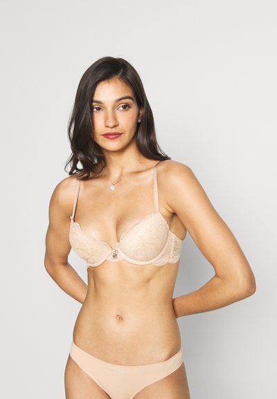 Sutien din dantelă în nuanță nud cu suport din sârma, având un model floral delicat, detaliu cu funda în centru și bretele ajustabile.