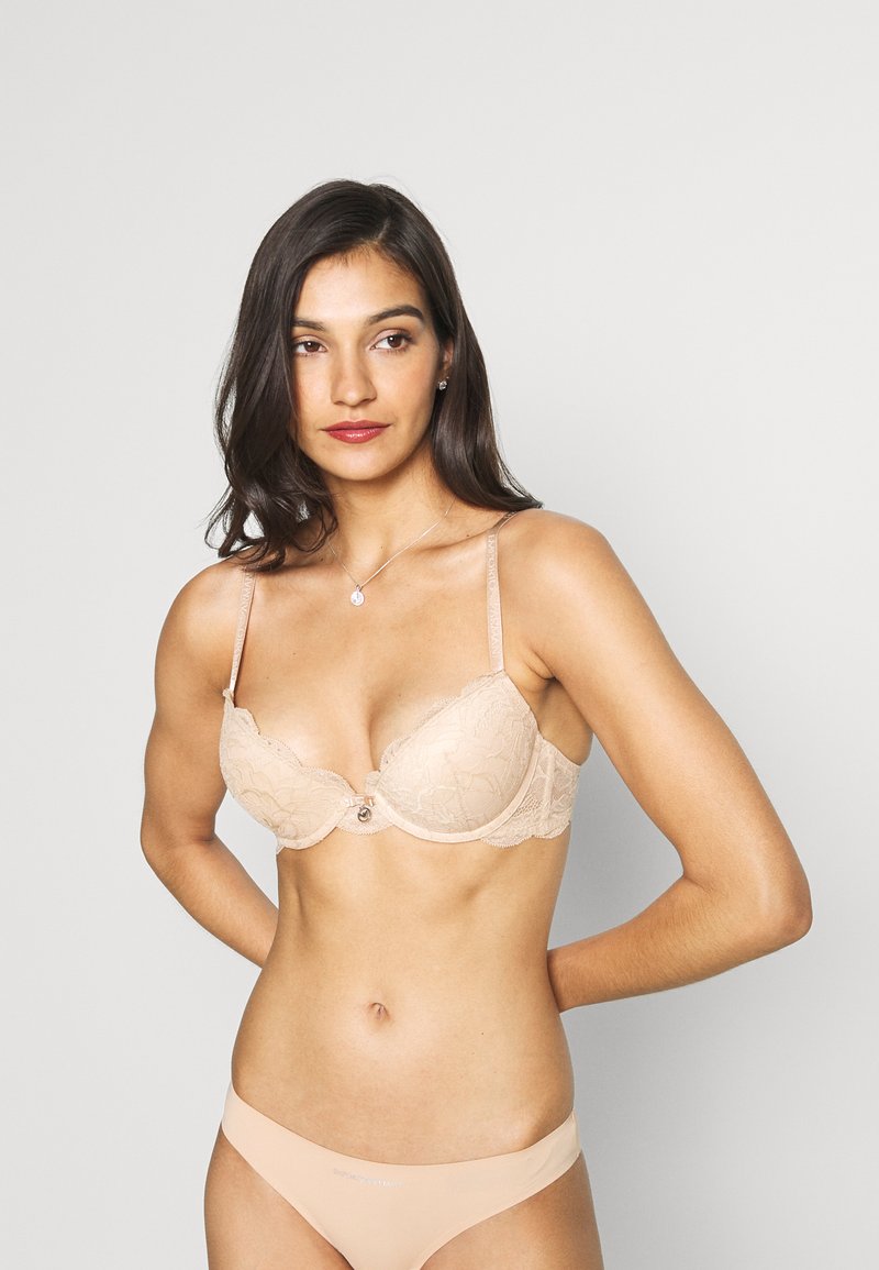 Lace bra in nude with underwire support, featuring a delicate floral pattern, bow detail at the center, and adjustable straps.