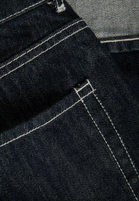 Sötétkék farmeranyag fehér varrással, közelről ábrázolva átfedő farmerzsebeket és varrásokat.