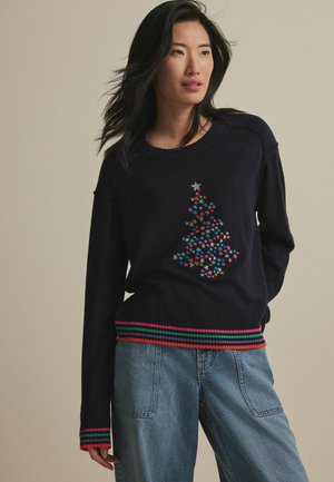 Marineblauer Pullover mit einem gestrickten Weihnachtsbaum-Motiv, das mehrfarbige Sterne zeigt. Rippbündchen mit roten, grünen und rosa Streifen.