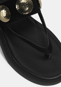 Schwarze Flip-Flop-Sandale mit breitem Riemen, der mit drei geschlagenen goldenen runden Akzenten verziert ist, texturiertem Fußbett und dünnem Zehensteg.