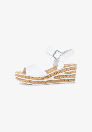 Sandales compensées blanches avec une plateforme à texture de liège, dotées d'une large bride au niveau des orteils, d'une bride à la cheville avec une boucle métallique et d'accents en design découpé.