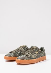 Kamouflage sneakers med en blandning av gröna nyanser, gummisulor med en orange ton och runda snören. Prägling av logotypdetalj på sidan.