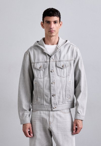 Lys grå denimjakke med hætte, der har to brystlommer, forknapper og synlige syninger. Glat tekstur og afslappet design.