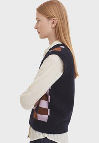 Mörkblå ärmlös väst med ett grafiskt mönster i rosa, brunt och lavendel. Mjuk textur med ribbade kanter och avslappnad passform.
