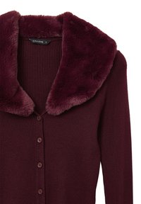 Cardigan bordeaux a coste con colletto in pelliccia sintetica, caratterizzato da una chiusura frontale con bottoni e maniche aderenti. Texture morbida e aspetto caldo.