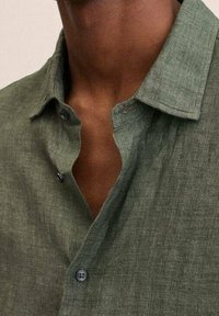 Grünes Leinenhemd mit lässigem Kragen, strukturiertem Stoff, zwei Knöpfen am Hals und lockerem Schnitt.
