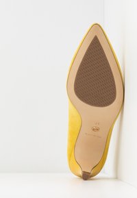 Chaussure à talon haut en daim jaune avec un bout pointu et une semelle en caoutchouc brun texturée. Taille 37 indiquée sur la semelle intérieure.