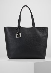 Svart totebag laget av preget syntetisk materiale, med merkevarenavnet i et gjentakende mønster, to solide håndtak og en sølvfarget logoetikett.
