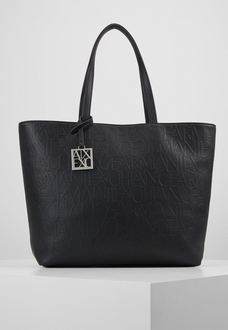 Svart totebag laget av preget syntetisk materiale, med merkevarenavnet i et gjentakende mønster, to solide håndtak og en sølvfarget logoetikett.