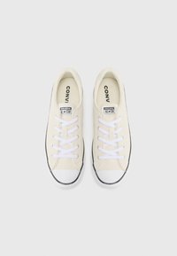 Beige canvas sneakers with white laces, rubber toe caps, and black soles. Features "Converse All Star" branding on the tongue.