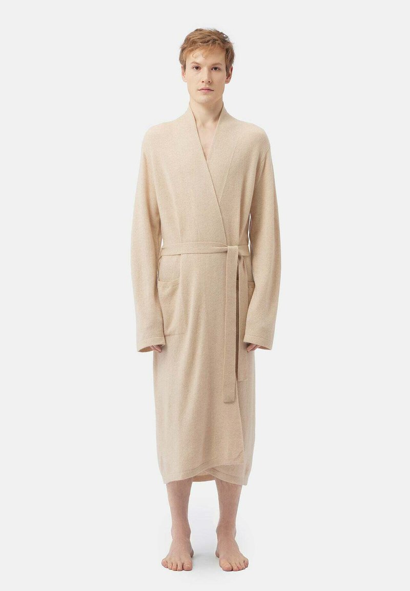 Beige badrock i mjukt tyg med långa ärmar, en omslagdesign och ett knytbälte i midjan. Två sidofickor synliga.