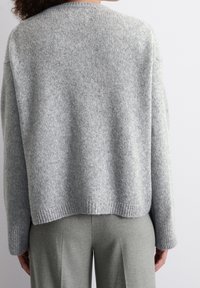 Pull gris en tricot avec ourlet côtelé, coupe décontractée, épaules tombantes et texture douce, associé à un pantalon gris clair.
