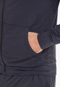 Marinblå zip-up huvtröja med framfickor, långa ärmar och ribbade muddar. Mjuk, slät tyg med en figursydd design för komfort.