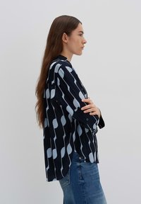 Zwarte en lichtblauwe geblokte blouse met lange mouwen en knoopsluitingen, met een losse pasvorm en een verticaal gestreept ontwerp.